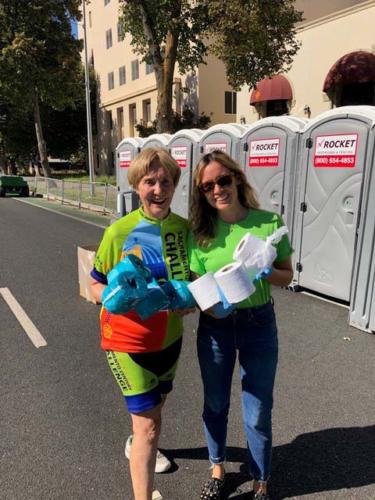 Two women carry toilet paper rolls as volunteers in an outdoor event