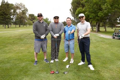 Four men stand on a golf course holding golf clubs
