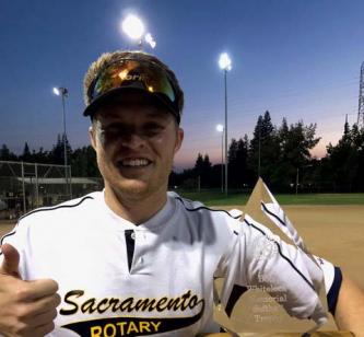 A young man in a Sacramento Rotary team shirt poses with a softball trophy and a thumbs up